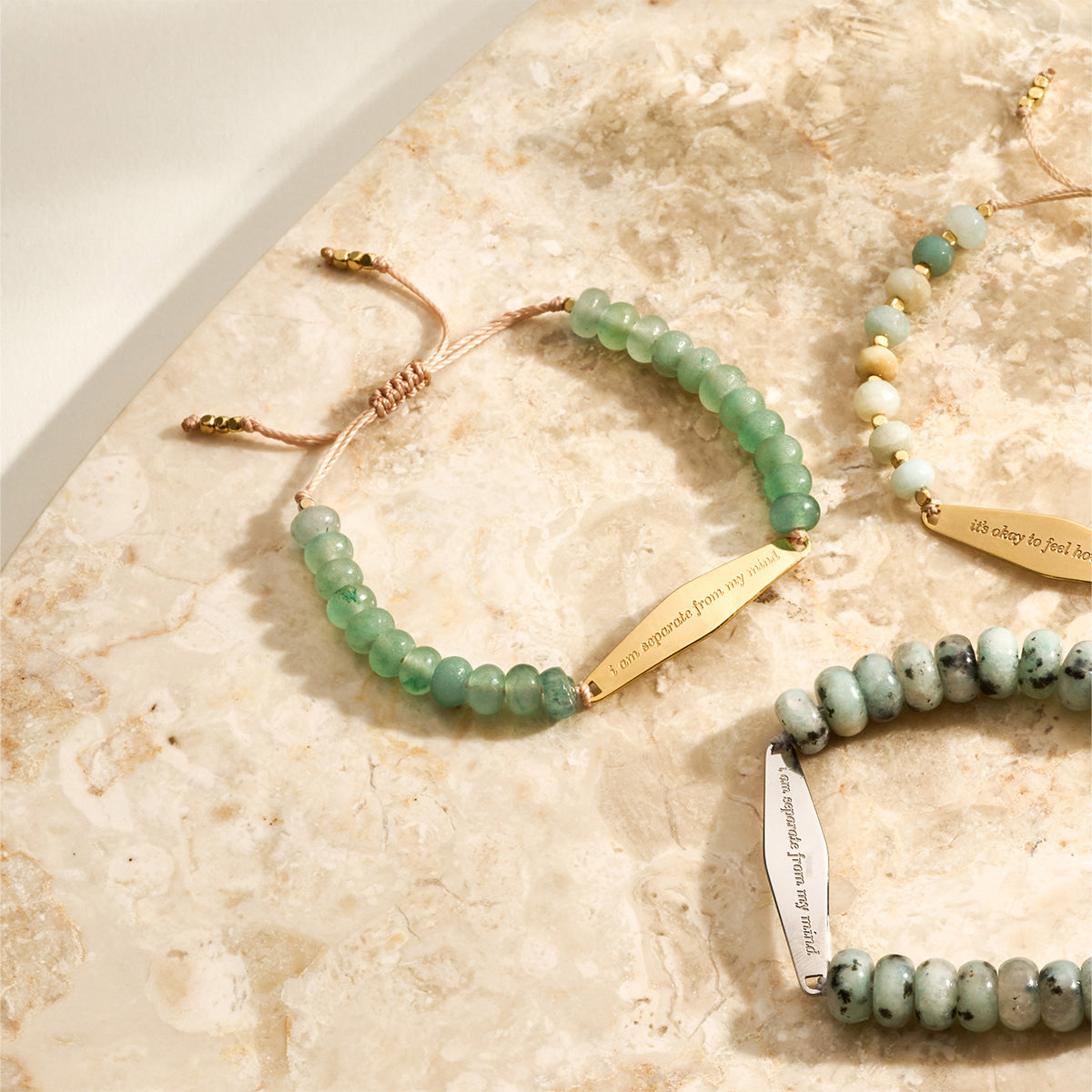 Close-up of an Aventurine gemstone bracelet next to other beaded bracelets from Presently's collection, showcasing the engraved phrase