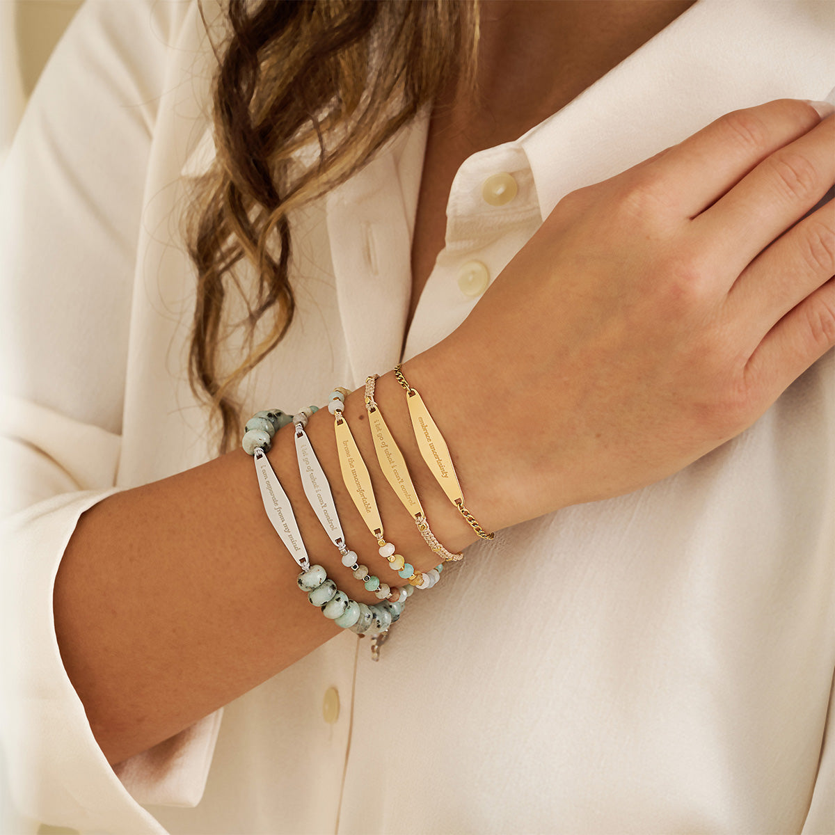 A model wearing a stack of five Presently bracelets, each engraved with phrases for managing OCD and anxiety, including