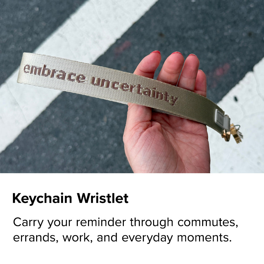 Keychain Wristlet. “Embrace Uncertainty” embroidered wristlet held over a crosswalk. Carry your reminder through commutes, errands, work, and everyday moments.