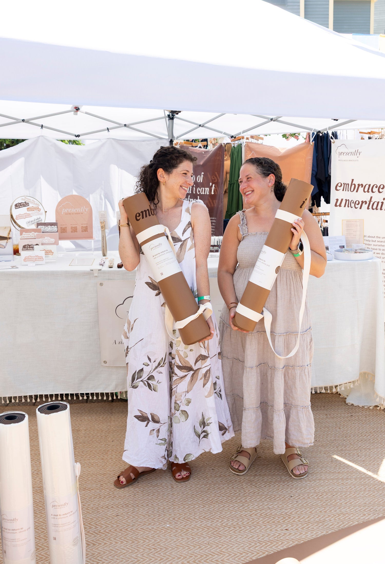 Presently co-founders and sisters holding rolled therapy-inspired yoga mats at their outdoor market booth