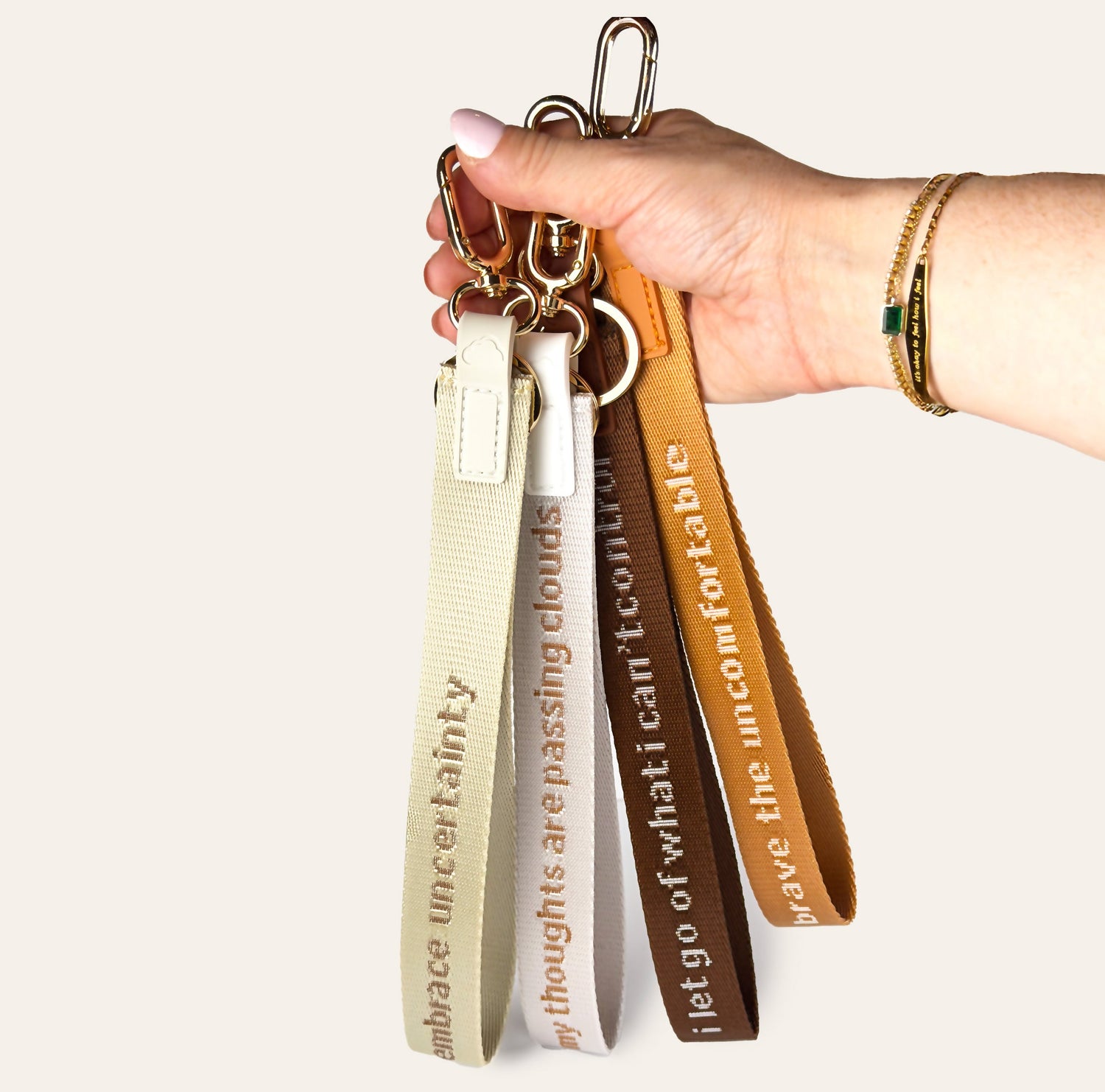 Hand holding a keychain with multiple straps featuring motivational phrases on a white background.