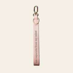 A light pink fabric keychain strap with a silver metal lobster clasp and D-ring, featuring the text 'I am separate from my mind' printed vertically in a darker pink tone, set against a solid off-white background.