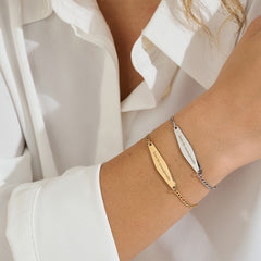 A model layering both gold and silver Figaro Chain Bracelets engraved with "Brave the uncomfortable," demonstrating their versatility.