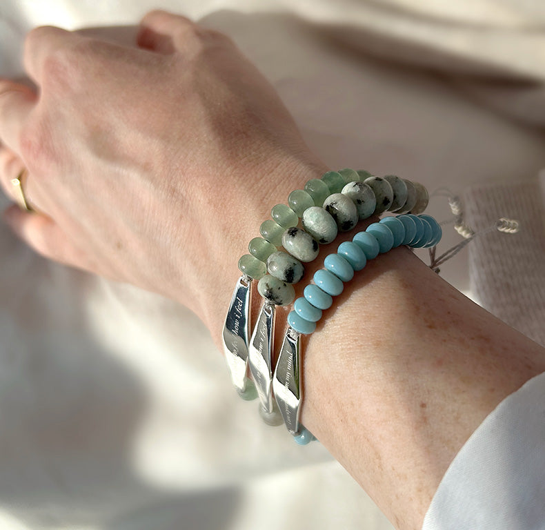 A customer wearing silver aventurine jade bracelet engraved with the phrase "it's okay to feel how i feel," along with other bracelets.