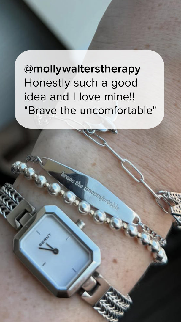 Silver “Brave the Uncomfortable” engraved reminder bracelet worn with layered jewelry. Customer quote reads, “Honestly such a good idea and I love mine!”