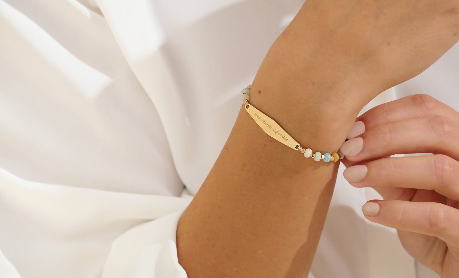 Gold engraved “Brave the Uncomfortable” gemstone reminder bracelet worn on wrist