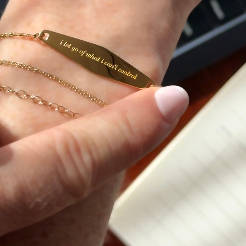 Gold engraved “I Let Go of What I Can’t Control” chain reminder bracelet held in hand