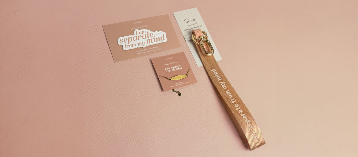A peach-colored keychain wristlet, mirror decal, and gold bracelet featuring the reminder “i am separate from my mind” on a textured light pink background.