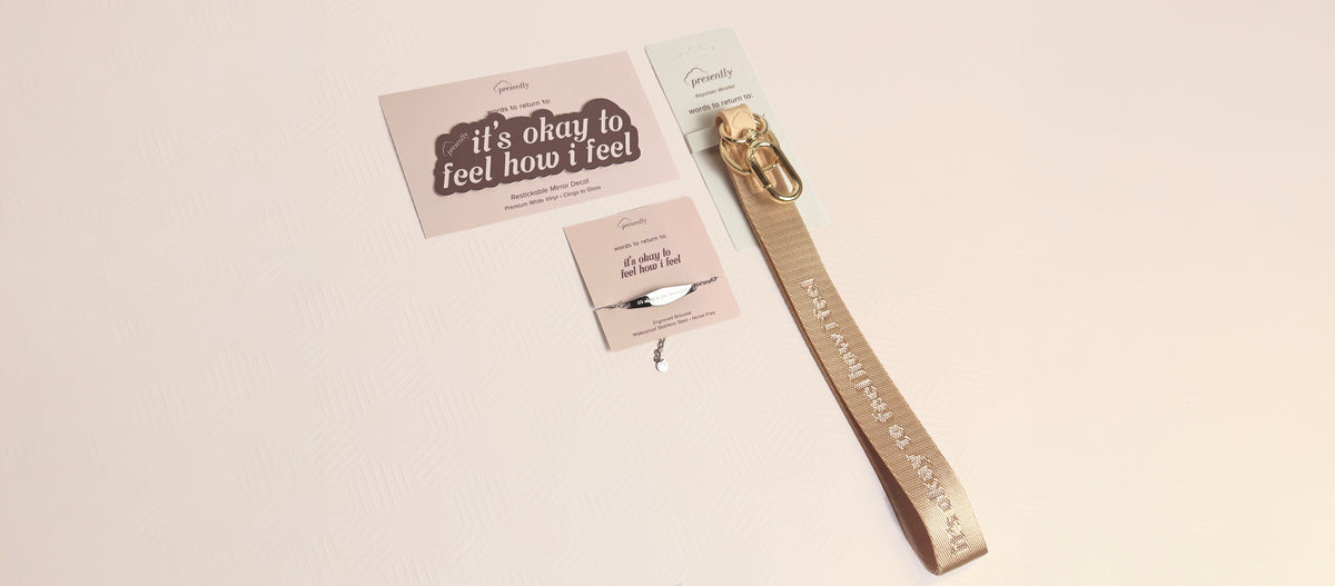 A light pink keychain wristlet, mirror decal, and silver bracelet featuring the reminder “it's okay to feel how i feel” on a textured light pink background.