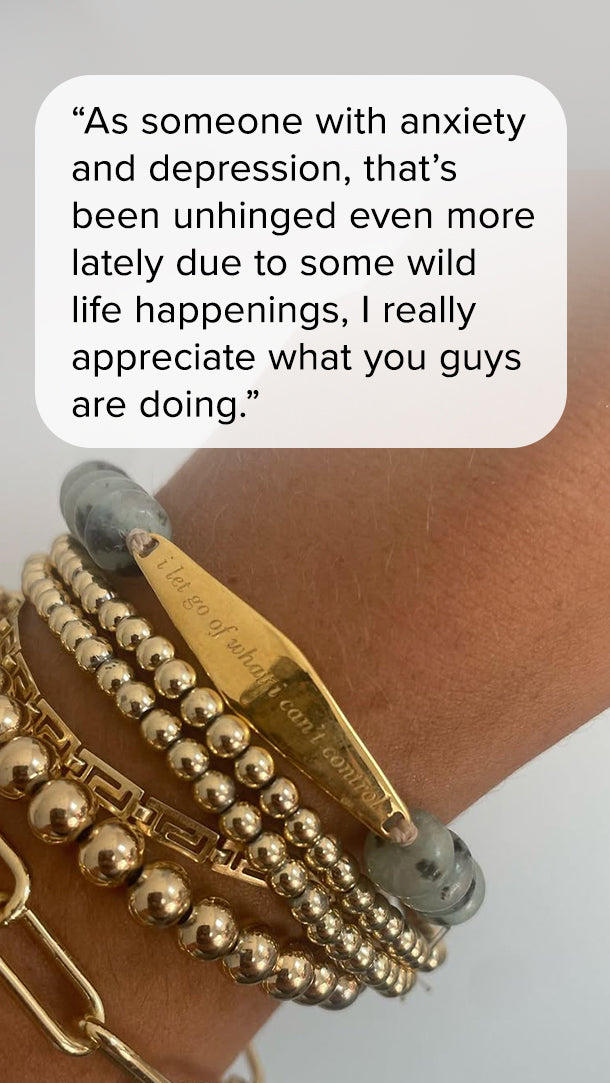Gold “I Let Go of What I Can’t Control” gemstone reminder bracelet worn with layered gold jewelry. Customer quote reads, “As someone with anxiety and depression, I really appreciate what you guys are doing.”