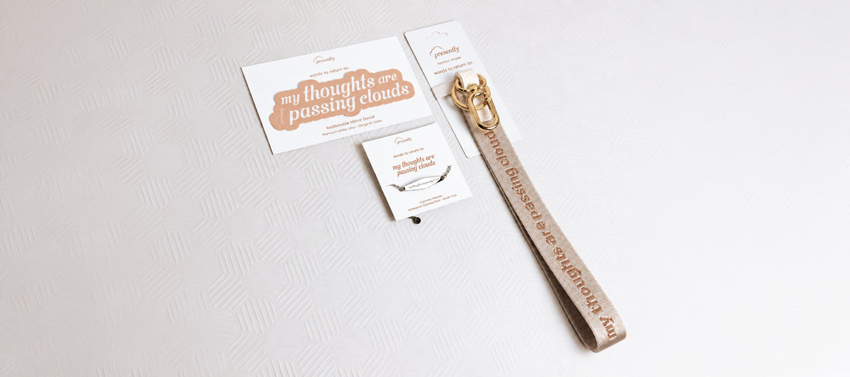 A beige keychain wristlet, mirror decal, and gold bracelet featuring the reminder “my thoughts are passing clouds” on a textured light beige background.